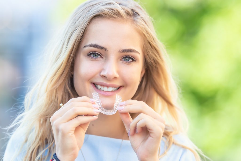 young blonde woman holding up Invisalign